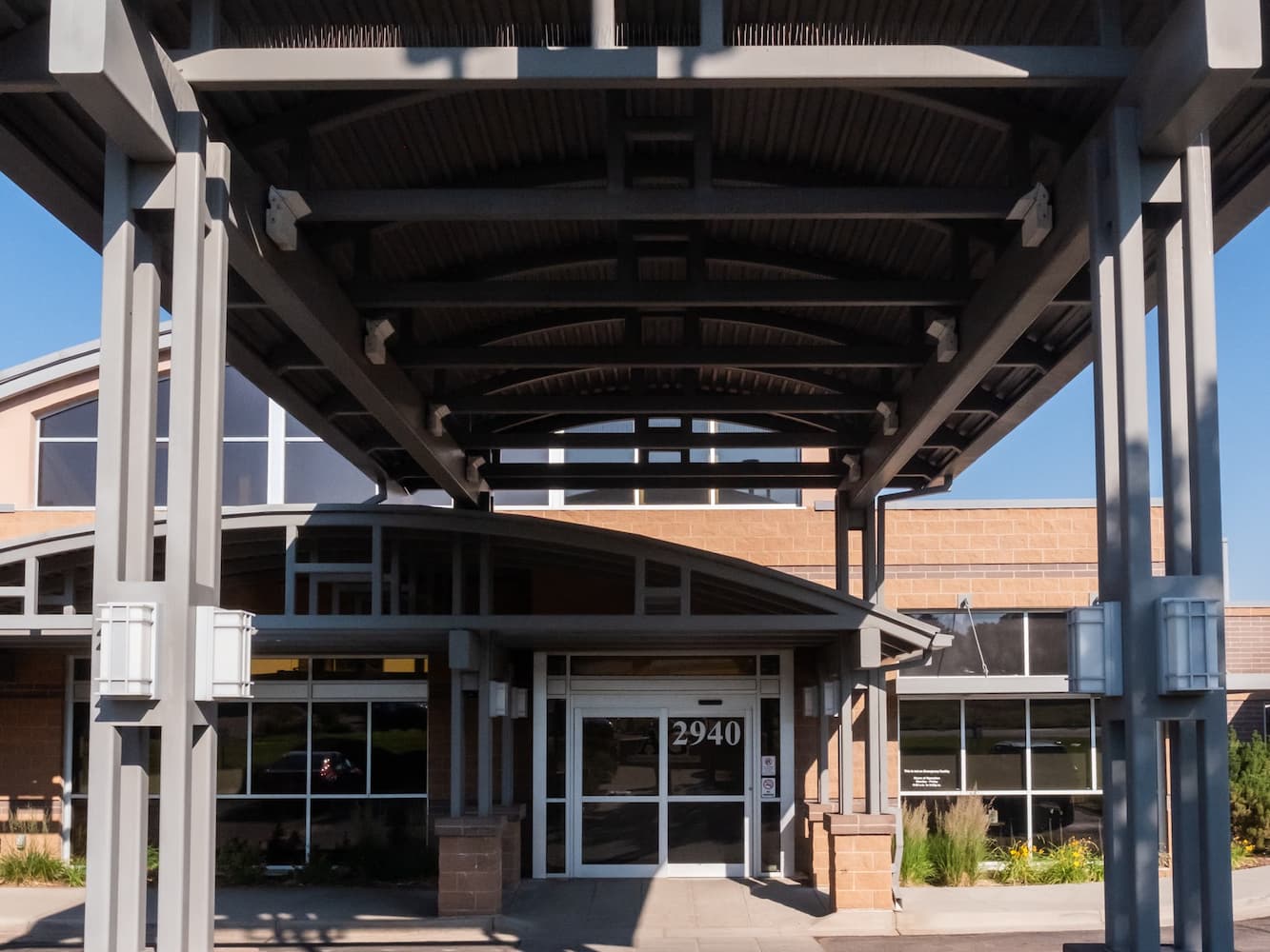 Entrance to a building with a large metal canopy and the address number 2940 on the glass door.