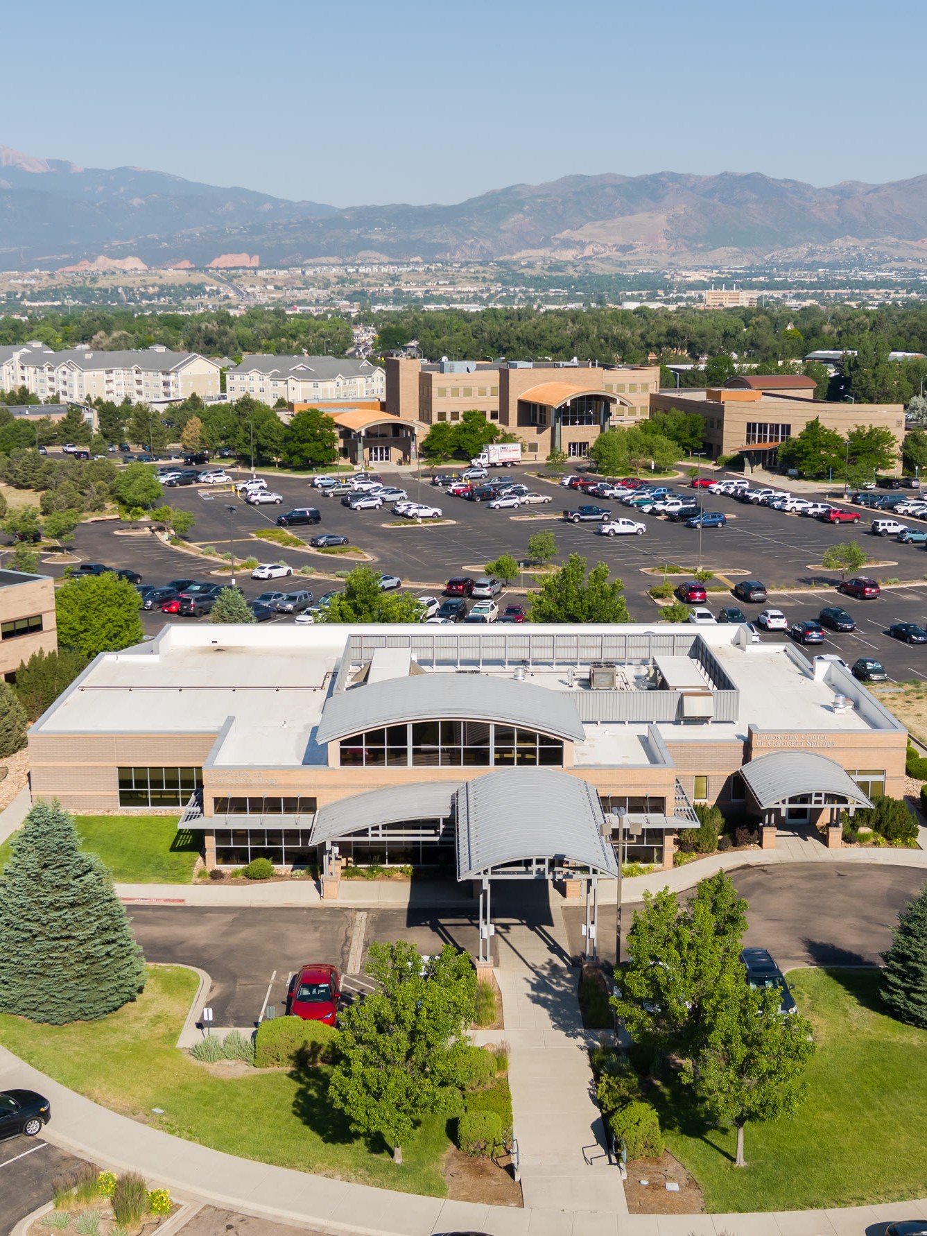 An aerial view of a tan commercial building complex with large parking lots, set against a backdrop of mountains.