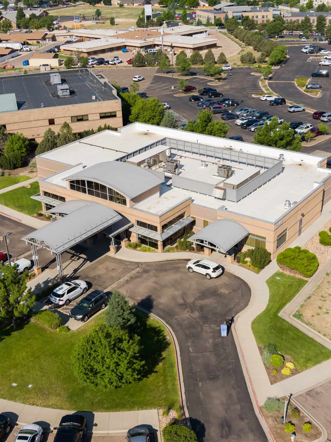 An aerial view of a single-story commercial building with a curved metal roof over the entrance and a parking lot.