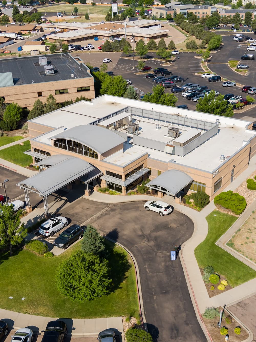 Aerial view of a suburban office building with a curved roof entrance, a drop-off loop, and a surrounding parking lot.