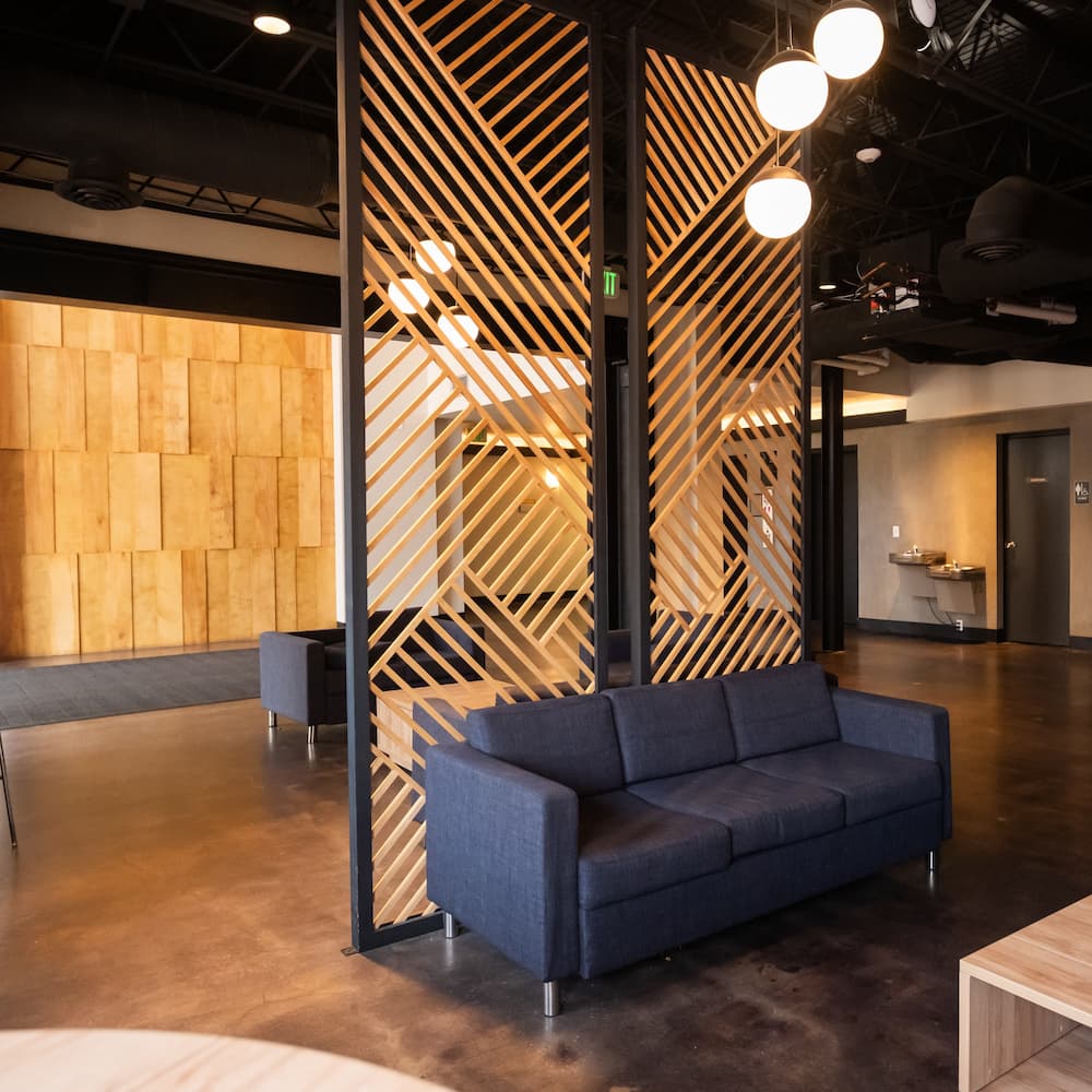 A dark blue sofa sits in front of a decorative wooden slat room divider in a modern office lobby.