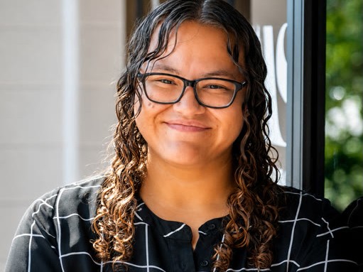 A person with curly hair and glasses smiling at the camera.