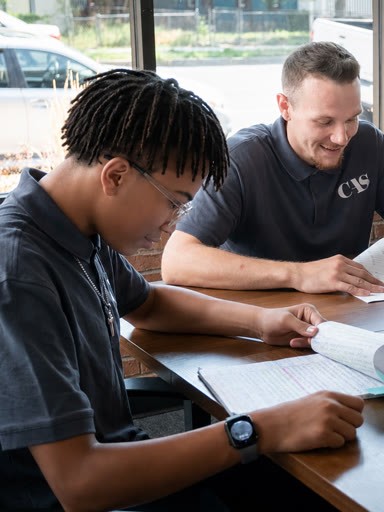 Two people in gray polo shirts sitting at a table looking at open notebooks.