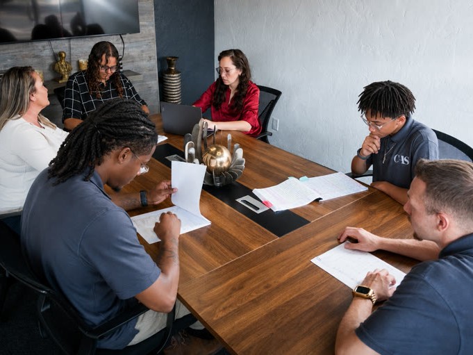Six people sitting around a conference table working with documents and laptops.