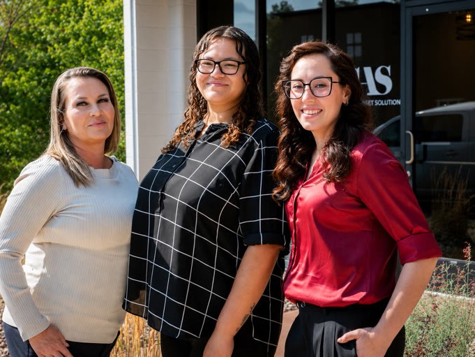 Three women standing together outdoors in front of an office building.