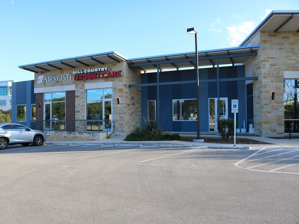 Exterior of a Hill Country Airrosti Urgent Care clinic with a parking lot in the foreground.